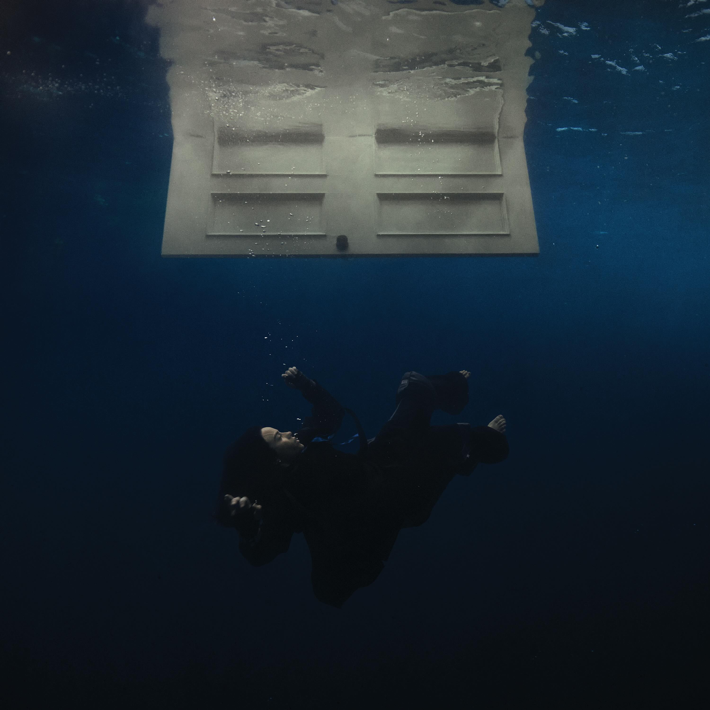 Billie Eilish floating beneath a white door in deep blue water